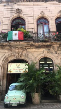 an old car parked in front of a building with flags on the balconies