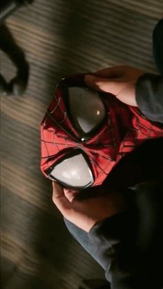 a spiderman mask is held in someone's hand while they sit on the floor