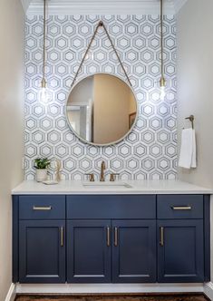 a bathroom with blue cabinets and a round mirror on the wall above it, along with a gold faucet