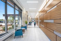 two people walking down a long hallway in a building with large windows on both sides