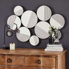 a wooden dresser topped with lots of mirrors next to a wall mounted lamp and vase