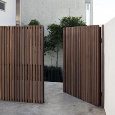 two wooden gates are open in front of a white building with a tree on the other side