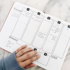 a woman's hand holding onto a planner on top of a marble countertop