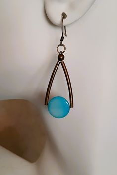 a pair of earrings hanging from a hook on a white surface with a light blue bead