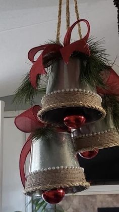 three bells are hanging from the ceiling with red bows and pine cones on them,