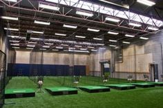 an indoor batting cage with artificial turf and lights on the ceiling is set up for practice