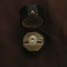 an engagement ring in a black box on top of a brown cloth covered tablecloth