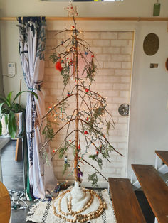 a small christmas tree in the corner of a room next to a brick wall and wooden table