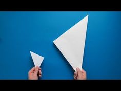 someone is holding two white paper airplanes on a blue surface with one pointing at the other