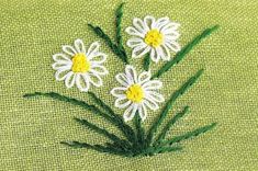 three white daisies with green stems on a green background, in the middle of an embroidered design