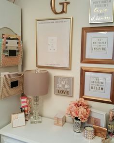 a white desk topped with lots of framed pictures and vases filled with flowers next to a lamp