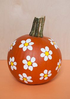 a painted pumpkin sitting on top of a table next to a wooden stick and orange wall