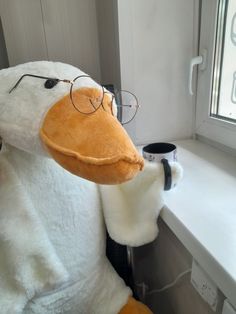 a stuffed duck with glasses sitting next to a window