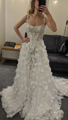 a woman taking a selfie in a wedding dress with flowers on the skirt and train