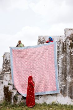 a woman standing next to a pink and blue blanket on top of a stone wall