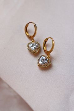 These elegant and timeless earrings feature sparkling CZ pave hearts, adding a touch of romance to any outfit. Crafted with precision and quality, these huggie earrings are perfect for any occasion. Materials: 14kt gold plated brass cz heart, gold plated brass huggie hoops SKU: E1631G Gold Cubic Zirconia Heart Earrings In Dainty Style, Gold Dainty Heart Earrings With Cubic Zirconia, Heart-shaped Gold Cubic Zirconia Earrings, Dainty Gold Heart Earrings With Cubic Zirconia, Elegant Gold Plated Huggie Earrings With Heart Charm, Gold Heart Cut Cubic Zirconia Earrings, Gold Heart Earrings With Diamond Accents For Wedding, Valentine's Day Cubic Zirconia Huggie Earrings, Elegant Huggie Earrings For Valentine's Day