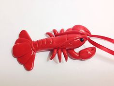 a red lobster ornament hanging from a red ribbon on a white table top