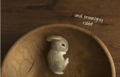 a small toy rabbit sitting in a wooden bowl on top of a wood table with words above it