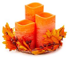 three orange candles with autumn leaves and berries