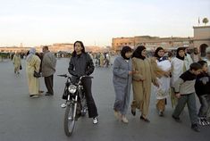 a woman standing next to a motorcycle in the middle of a street filled with people