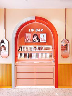 an orange and white display case with lipstick on the shelves in front of two mirrors