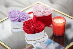 three roses in small boxes sitting on a glass table next to a red candle and some candles