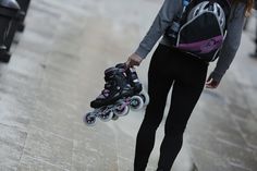 a woman walking down the street with roller skates in her hand and a backpack on her back