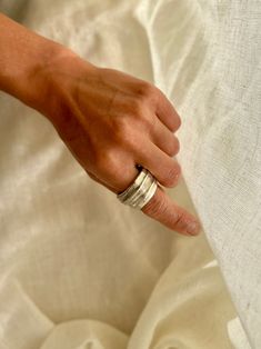 a woman's hand with two silver rings on her finger, resting against a white sheet