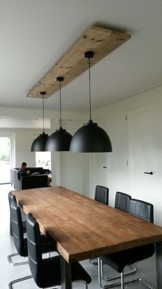 a wooden table surrounded by black chairs in a room with lights hanging from the ceiling