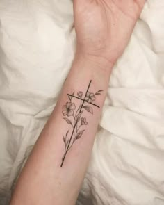 a woman's arm with a cross and flowers tattoo on the left side of her wrist