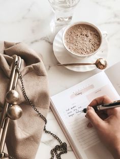 a person writing in a notebook next to a cup of coffee