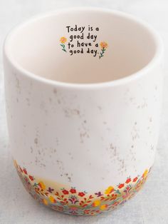 there is a white cup that has writing on the inside of it and colorful flowers