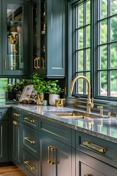 a kitchen with green cabinets and marble counter tops, gold pulls on the faucet