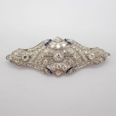 Edwardian era combination of a brooch and pendant in filigree designs made of platinum and decorated with Diamonds and Sapphires. There is one Old European cut diamond in the center, approx. 0.32ct, VS2 clarity, H color.  Side stones are approx. 0.52ctw, Old European cut, H-I color, SI1 clarity. Accented with 122 Old European cut diamonds: H-I color, SI clarity, approx. total weight is 4.4ct.  12 baguette cut synthetic sapphire stones are approx. 0.24ctw.  This majestic brooch or pendant is 67 mm long, 26 mm wide, weighing 14.14 grams. EA3840 Diamond Filigree Brooches As Gift, Ornate Diamond Brooches With Intricate Design, Vintage Platinum Brooches With Diamond Accents, Vintage Diamond Brooches With Filigree, Vintage Diamond Brooches Hallmarked, Baguette Cut, Filigree Design, Edwardian Era, European Cut Diamonds