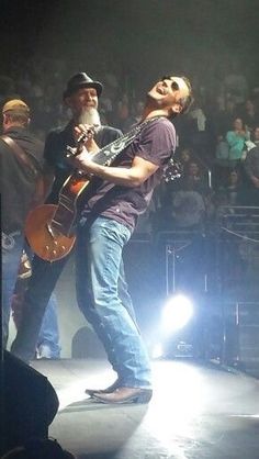 a man standing on top of a stage with a guitar in his hand and people behind him