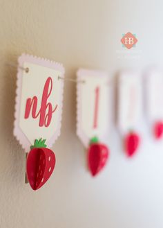 three red strawberries hanging from the side of a white wall next to each other