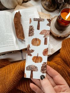 a person holding an open book in their hand with autumn leaves and acorns on it