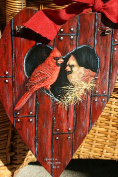 a wooden heart shaped ornament with two birds on it and a red bow