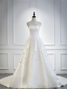 a white wedding dress is on display in front of a white wall and flooring