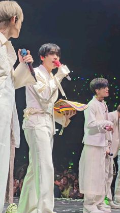 the group of young men are performing on stage with one holding a microphone and wearing white clothes