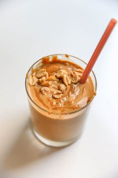 a glass filled with peanut butter and topped with a red plastic straw on top of a white table