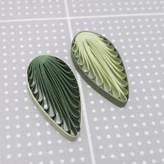 two green leaf shaped brooches sitting on top of a table