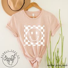 This happy hand-drawn smiley face with a checkered pattern is designed in a soft, cozy, lightweight t-shirt. We hope you like it! * 100% combed and ring-spun cotton (Heather colors contain polyester) * Fabric weight: 4.2 oz/yd² (142 g/m²) * Pre-shrunk fabric * Side-seamed construction * Shoulder-to-shoulder taping Refund/Exchange Policy: We do not accept returns or exchanges. Please refer to the sizing chart under the listed product to ensure you're selecting the best fit. Thank you! Casual Plaid T-shirt With Graphic Print, Trendy Smiley Face Tops For Everyday, Casual Gingham Crew Neck Top, Relaxed Fit Plaid Shirt With Graphic Print, Smiley Face Shirt, Minimal Gifts, Boho Tees, Happy Face, Checkered Pattern