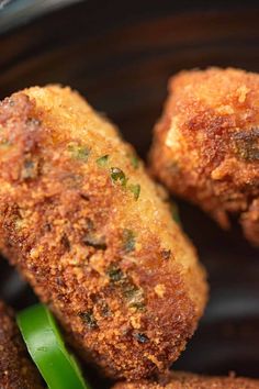 some fried food in a black bowl with green peppers on the side and two pieces of broccoli