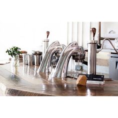 a row of stainless steel faucets sitting on top of a wooden countertop