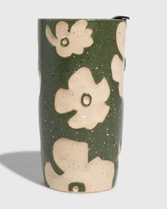 a green and white vase with flowers painted on it's sides, sitting against a gray background