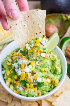 a hand dipping a tortilla chip into a bowl of guacamole