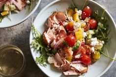 two white bowls filled with salad next to a glass of wine and some yellow flowers