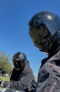 two people riding on the back of a motorcycle with their helmets up and facing each other