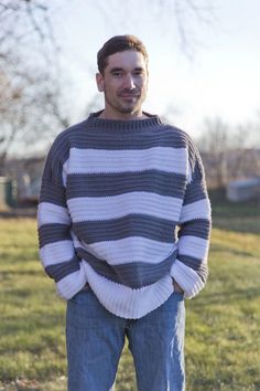 a man standing in the grass with his hands on his hips wearing a striped sweater